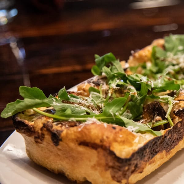 Close-up of a rectangular flatbread pizza topped with arugula, cheese, and balsamic glaze.