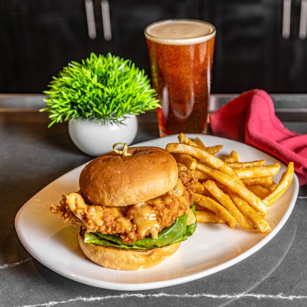 Crispy chicken sandwich with lettuce, sauce, and fries on a white plate with a beer.