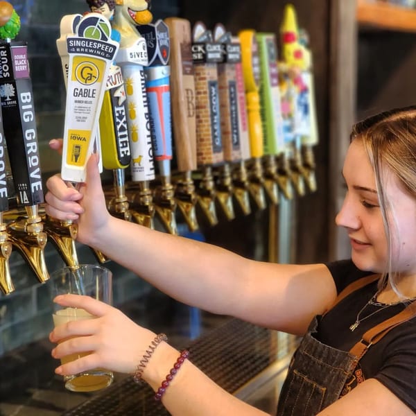 A bartender at Copper Boar American Pub pours a beer from a tap with many other taps visible.
