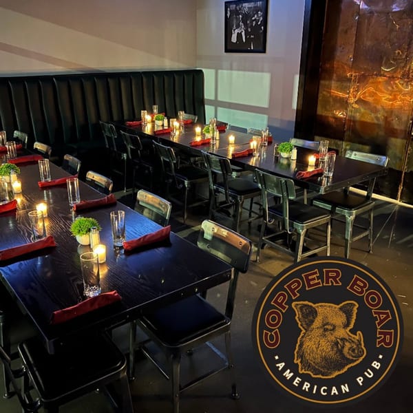 Long dining tables with red napkins, candles, and greenery, set against a dark booth and industrial wall.