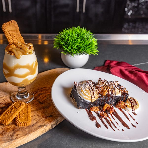 A rich chocolate brownie with toasted marshmallows, candied nuts, and chocolate drizzle, next to a caramel milkshake.